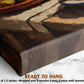 The image is a close-up of a wooden frame with a painting of a bowl of fruit on it, placed on a marble surface.