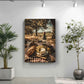 a large canvas print of a picnic scene, with a bottle of wine, bread, cheese, and grapes arranged on a checkered cloth. The print is hung on a white wall, with two potted plants placed on either side of it.