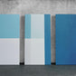 three blue and white pieces of art against a concrete wall