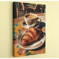 A croissant on a floral plate and a cup of coffee on a wooden table, with a wicker chair visible in the background.