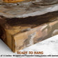 The image is a close-up of a wooden frame with a painting on it, placed on a marble surface.